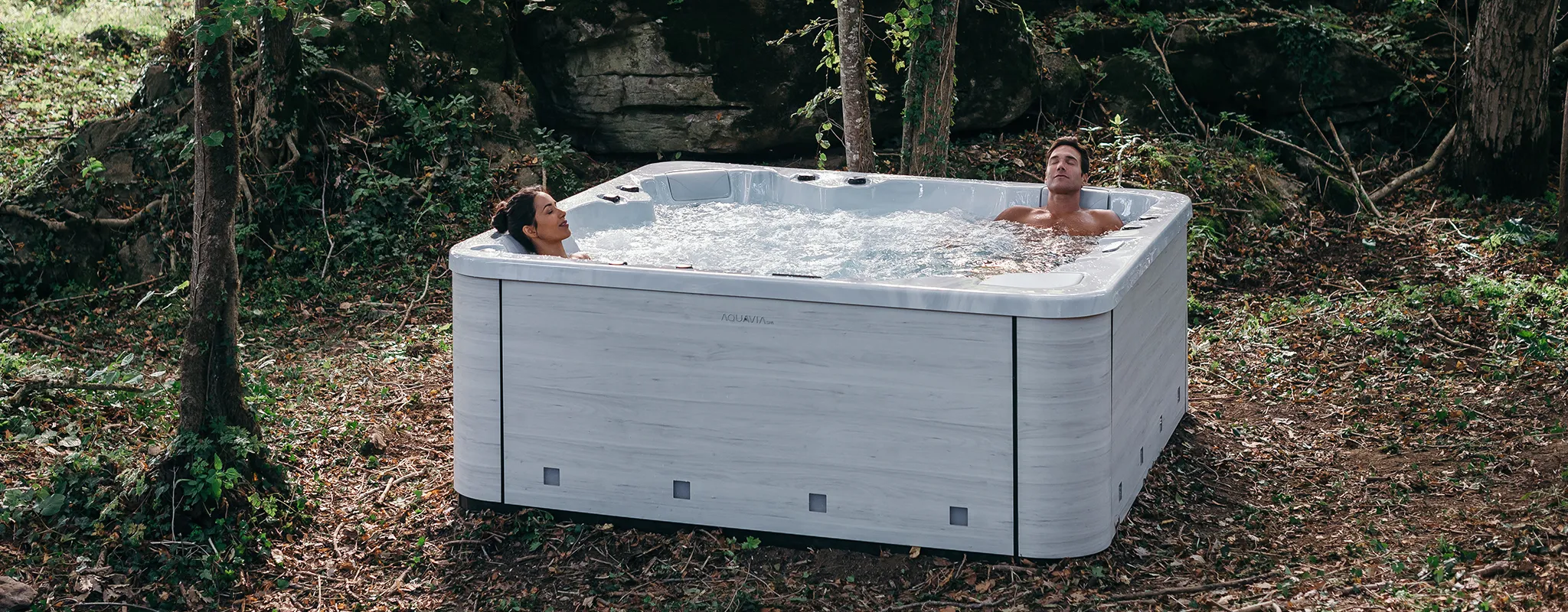 Para odpoczywająca w wannie z hydromasażem Aquavia Spa ustawionej w leśnym otoczeniu.