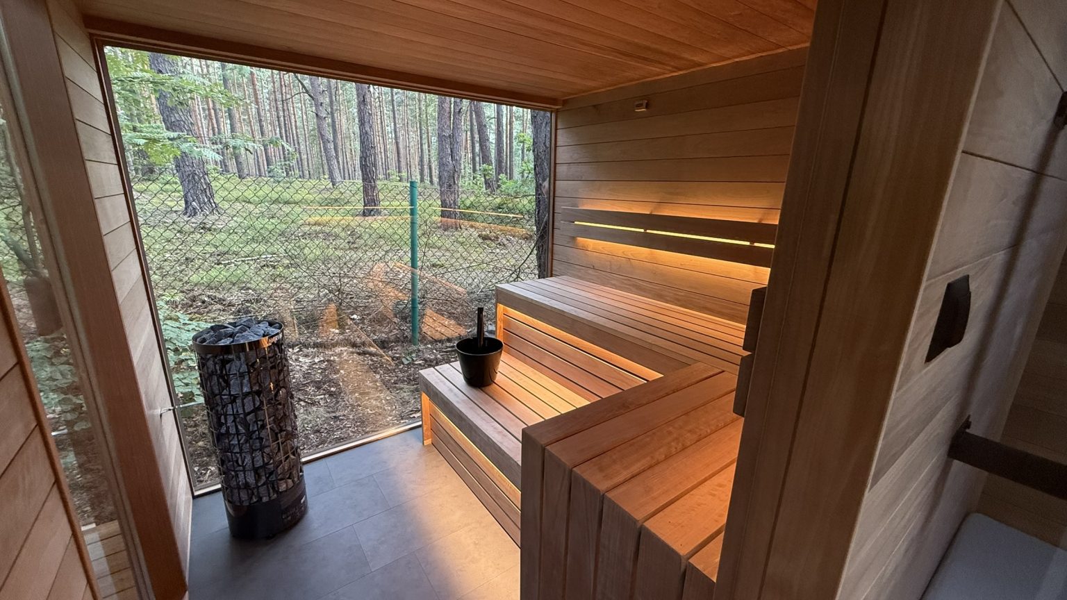 Wnętrze nowoczesnej sauny z widokiem na las przez duże przeszklenie.