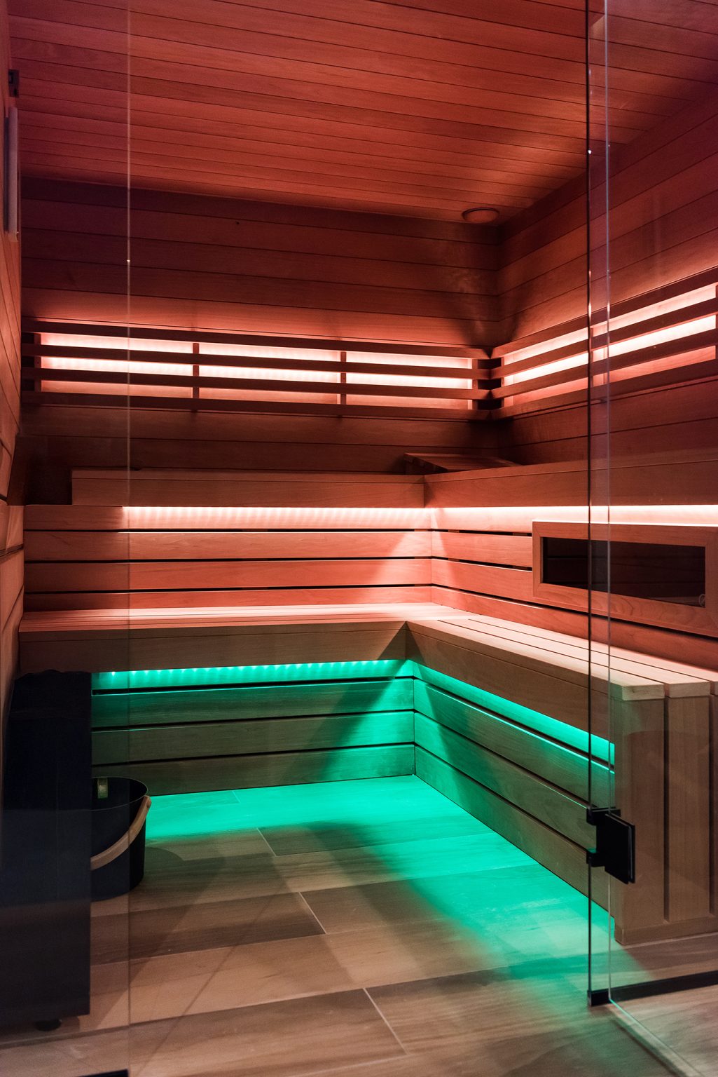 Wnętrze nowoczesnej sauny z drewnianymi ławami i oświetleniem LED w kolorach czerwonym oraz zielonym.