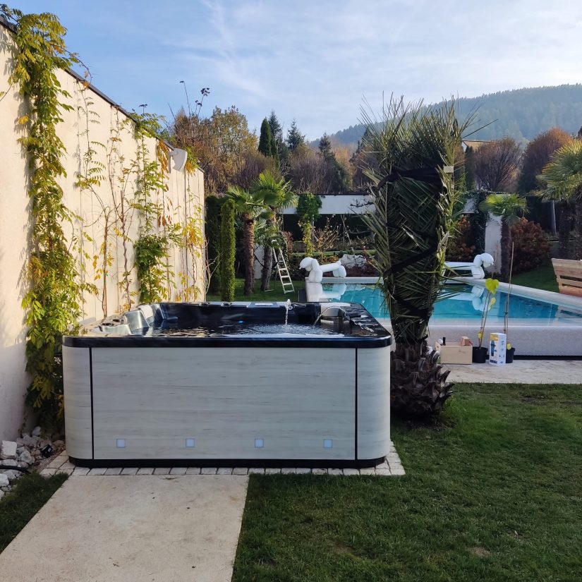 Wanna zewnętrzne w ogrodzie z basenem i roślinnością w tle.