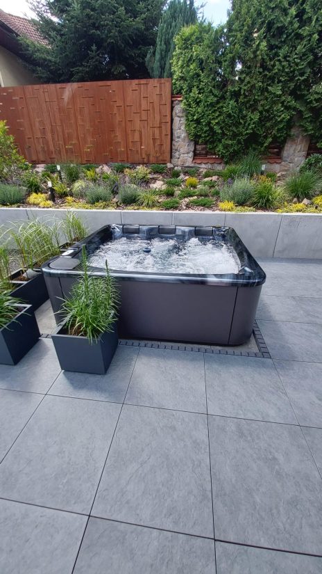 Wanna z hydromasażem na tarasie z nowoczesnym ogrodem w tle.