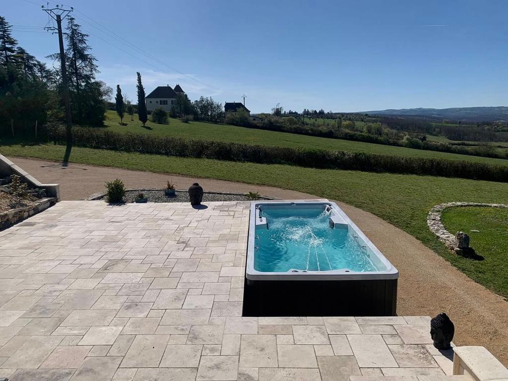 Jacuzzi ogrodowe z błękitną wodą na kamiennym tarasie z widokiem na zielone wzgórza.