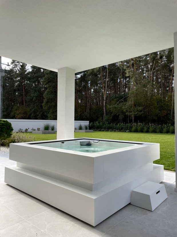 Białe jacuzzi na tarasie z widokiem na ogród i las.