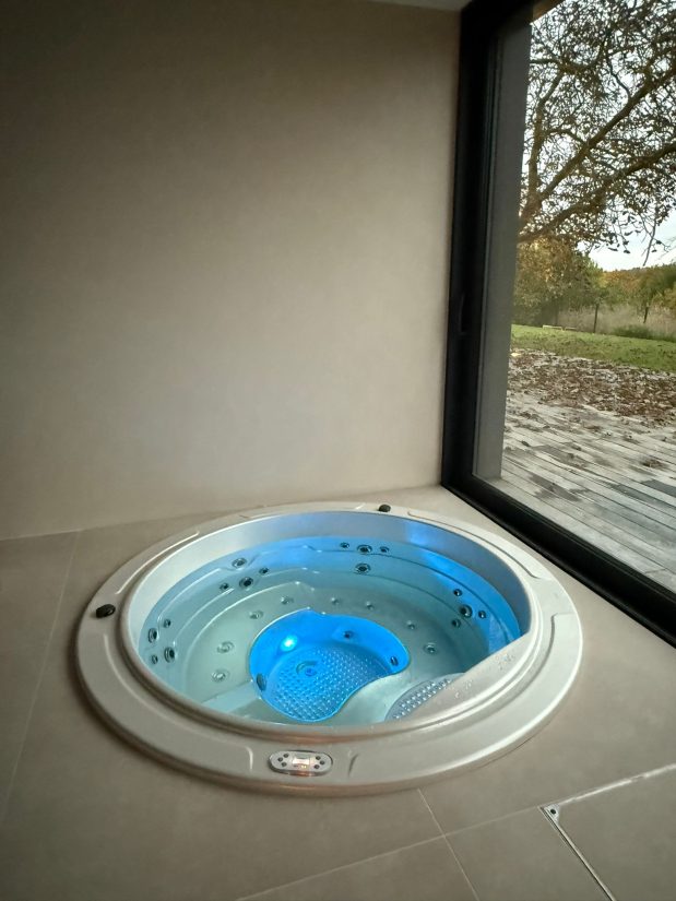 Wanna z hydromasażem z niebieskim podświetleniem przy oknie z widokiem na ogród.