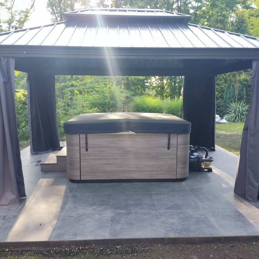 Zamknięte jacuzzi z pokrywą pod ogrodową altaną z zasłonami.