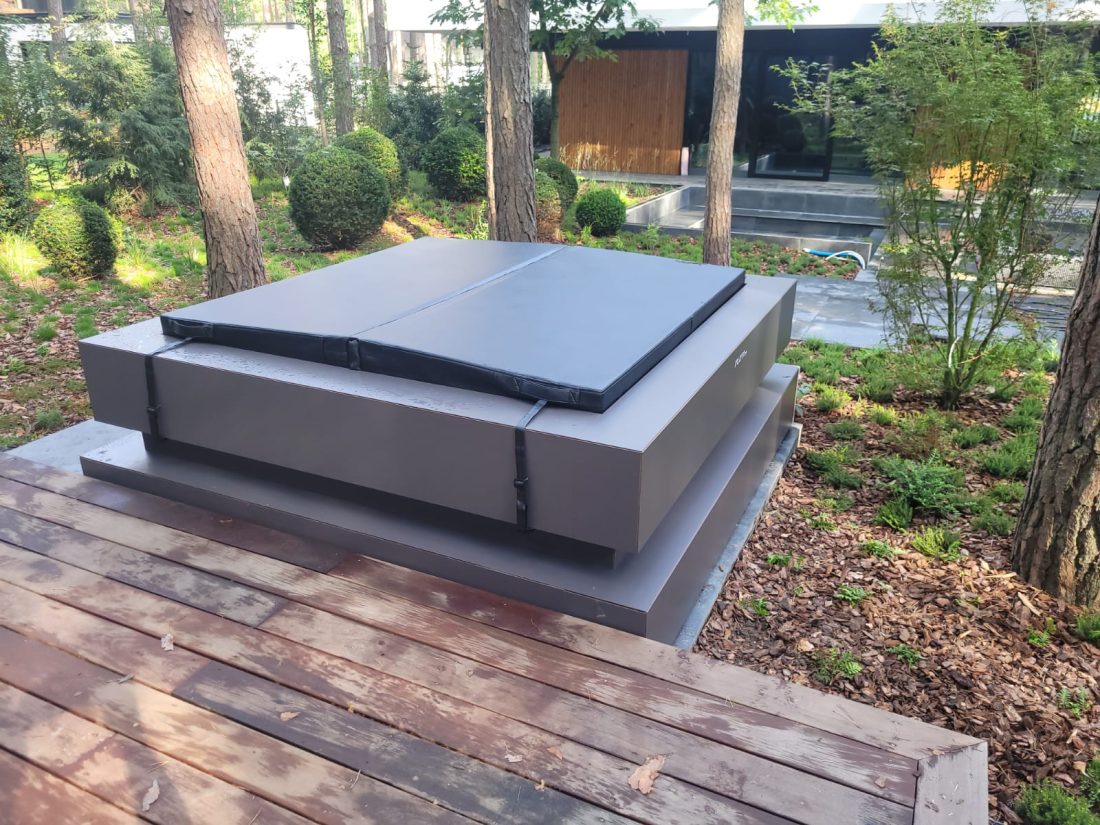 Zewnętrzne jacuzzi z zamkniętą pokrywą na drewnianym tarasie w ogrodzie.