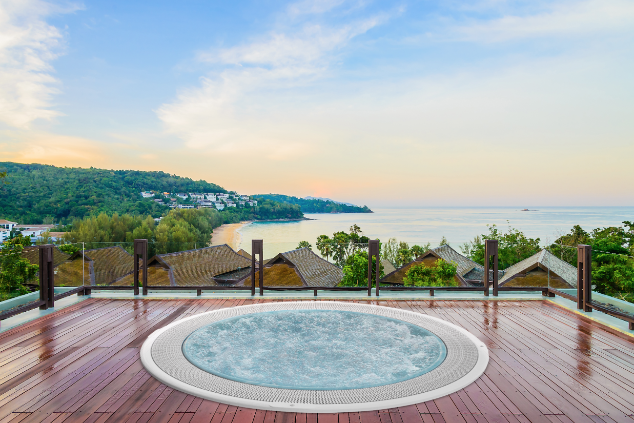 Okrągłe jacuzzi na drewnianym tarasie z widokiem na morze i tropikalne wybrzeże o zachodzie słońca.