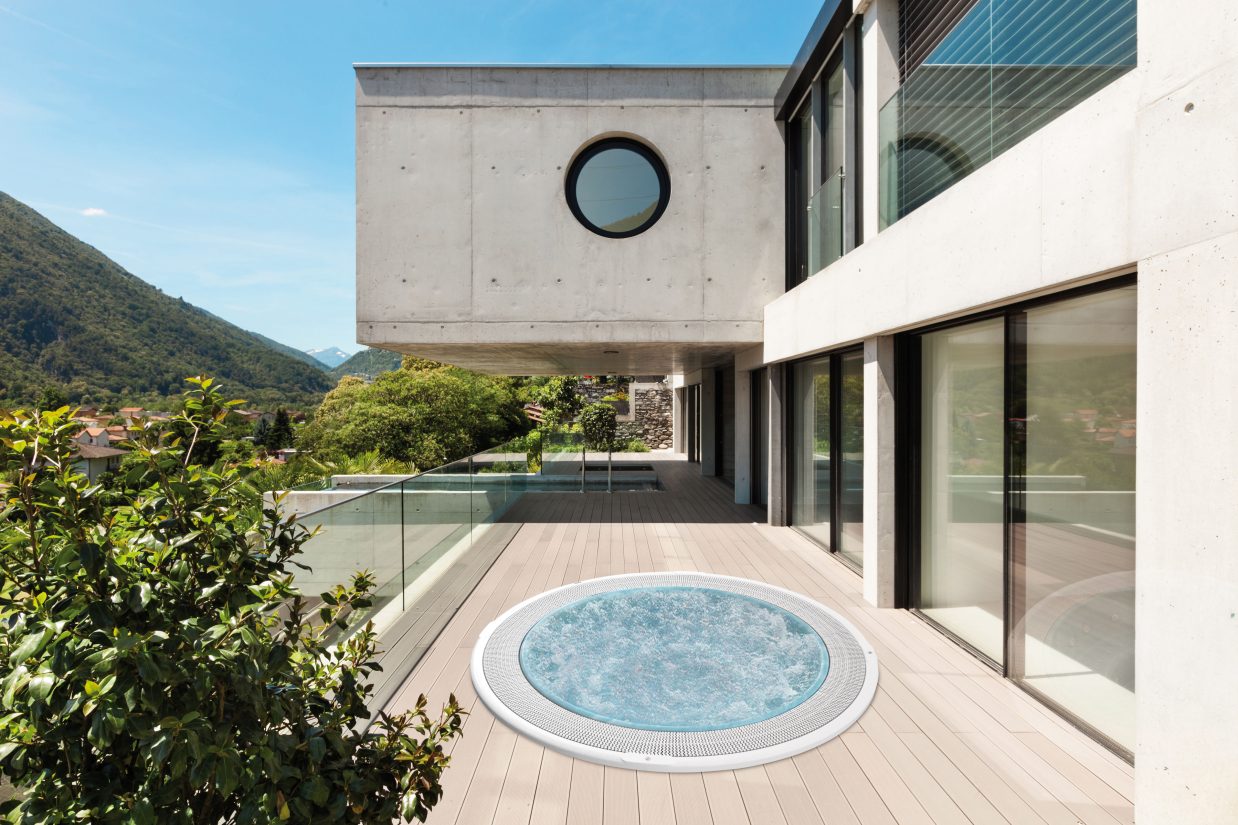 Nowoczesny taras z okrągłym jacuzzi na tle betonowej architektury i górskiego krajobrazu.