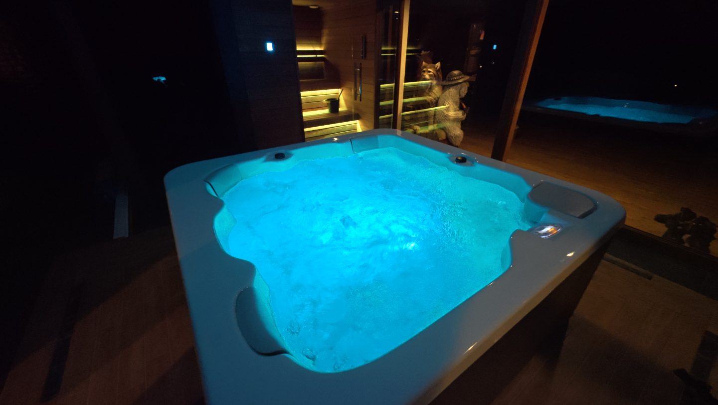 Podświetlane na niebiesko jacuzzi na tarasie przy saunie w nocy.