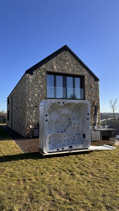 Nowa wanna spa ustawiona na drewnianym tarasie przed kamiennym domem.