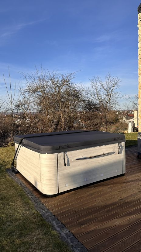 Zamknięte jacuzzi ogrodowe z jasną obudową na drewnianym tarasie.