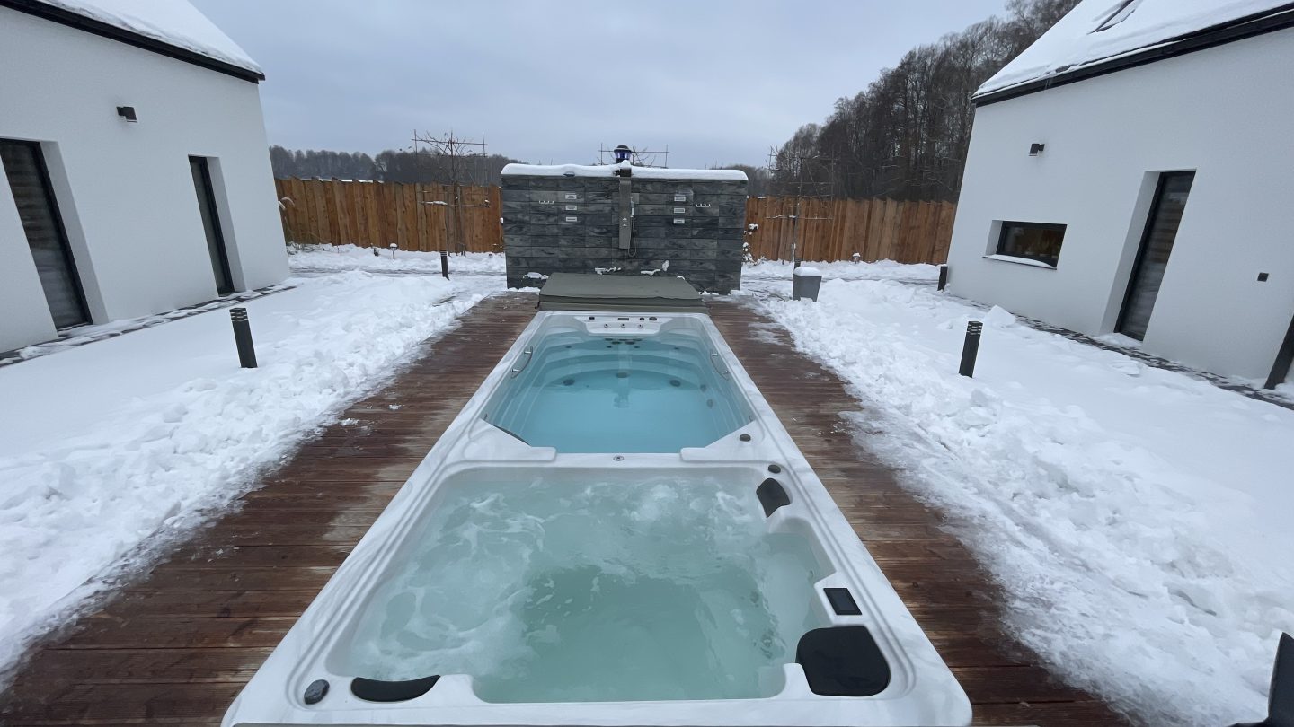 Basen typu swim spa na drewnianym tarasie w zimowej scenerii.