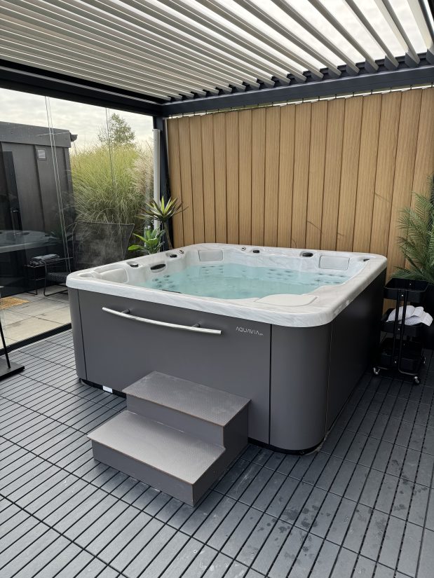 Wanna spa Aquavia na tarasie z drewnianą ścianą i zadaszeniem.
