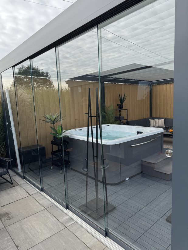 Jacuzzi w nowoczesnej zabudowie tarasowej ze szklanymi ścianami przesuwnymi.