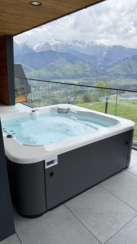 Jacuzzi na tarasie z widokiem na ośnieżone góry i dolinę.