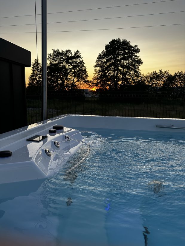 Woda tryskająca z dysz wanny spa podczas zachodu słońca na tle drzew.