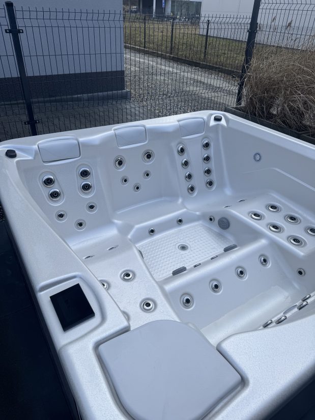 Biała wanna spa z hydromasażem i wieloma dyszami ustawiona na zewnątrz.