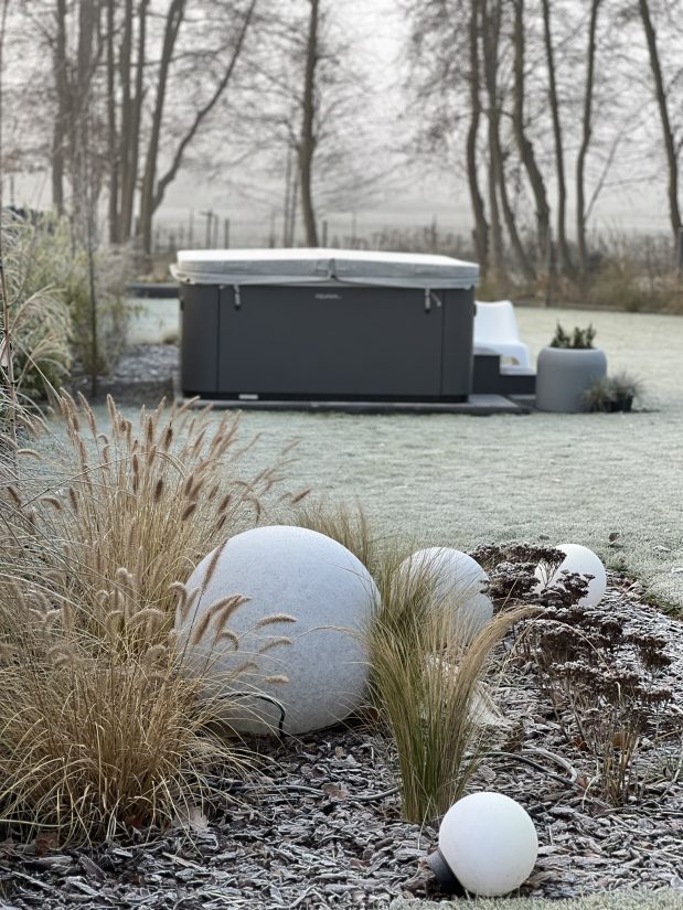 Zimowy ogród z przykrytą wanną spa i ozdobnymi podświetlanymi kulami na rabacie.