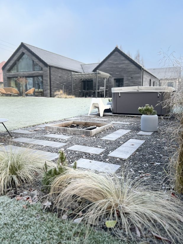 Nowoczesny dom z ogrodem, jacuzzi oraz miejscem na ognisko w mroźny, słoneczny dzień.