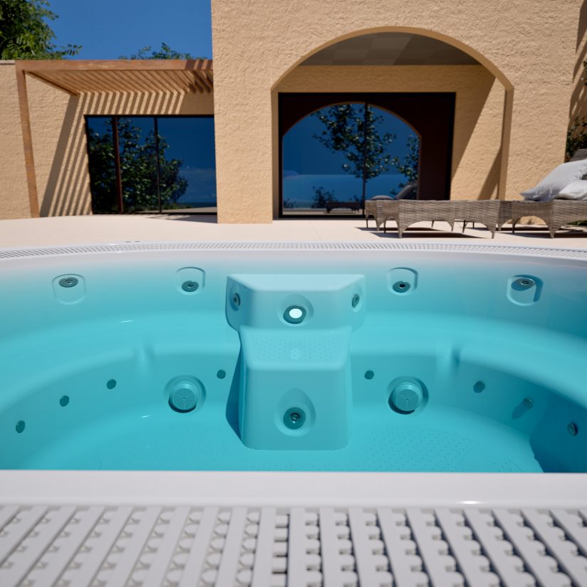 Puste wnętrze błękitnego jacuzzi na tle nowoczesnego domu z tarasem i leżakami.