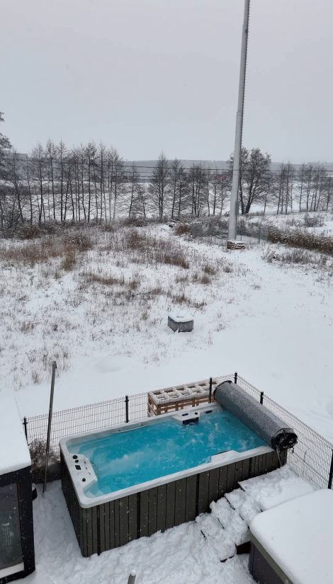 Ogród z jacuzzi z błękitną wodą podczas zimowych opadów śniegu.