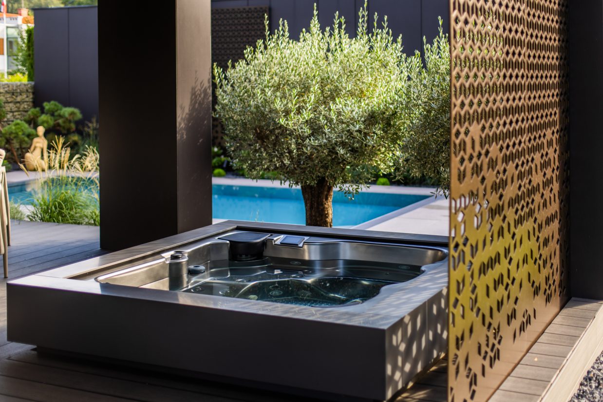 Wanna zewnętrzna z hydromasażem na tarasie przy basenie i drzewie oliwnym.