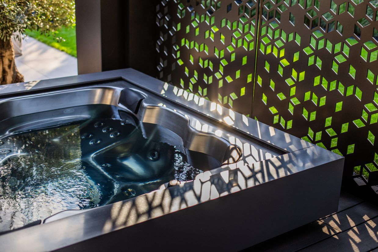 Nowoczesne jacuzzi ogrodowe obok ażurowego panelu dekoracyjnego.