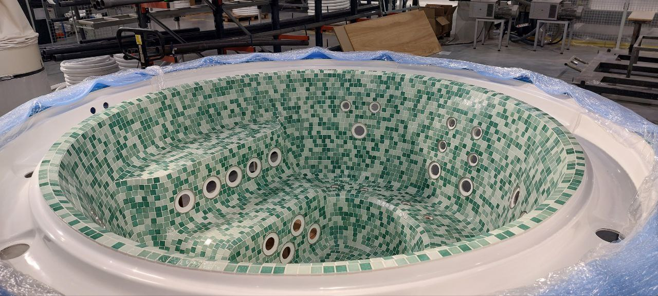 Okrągła wanna z hydromasażem wyłożona zielono-białą mozaiką w hali produkcyjnej.