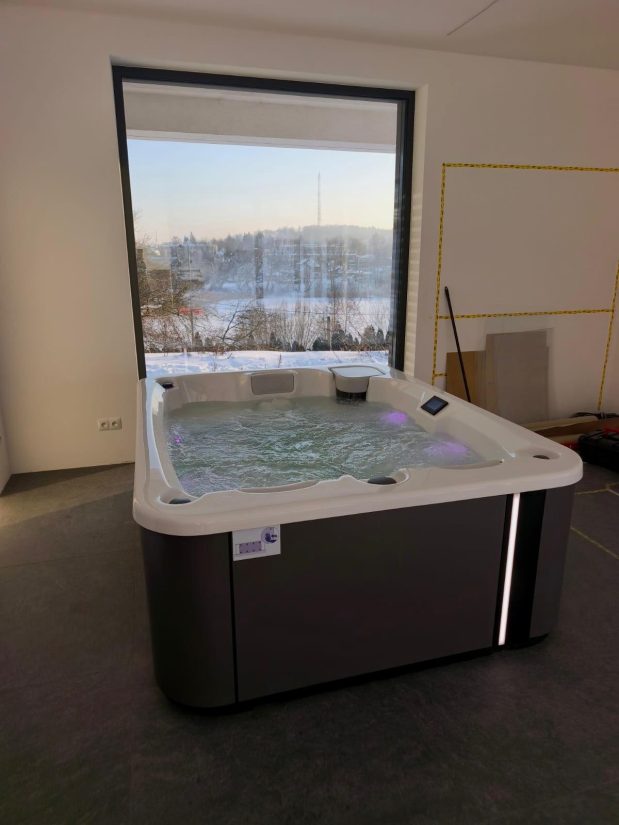 Wanna jacuzzi z hydromasażem przy dużym oknie z widokiem na zaśnieżony krajobraz.