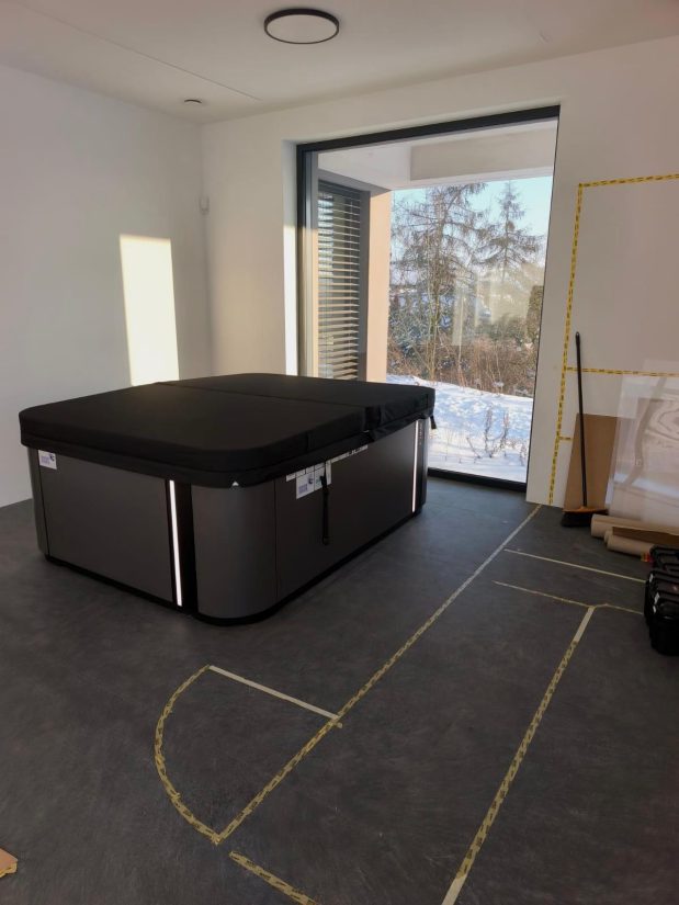 Zamknięta wanna spa z pokrywą w pomieszczeniu z dużym oknem wychodzącym na zaśnieżony ogród.