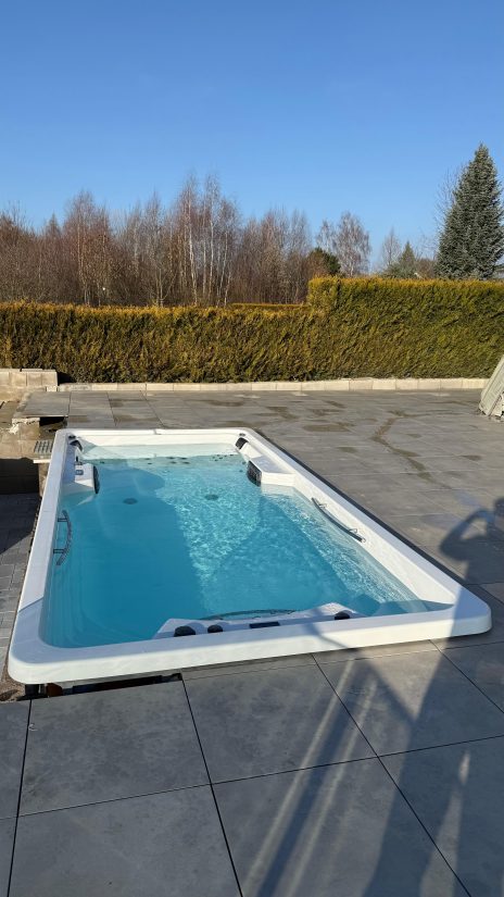 Wanna z hydromasażem typu swim spa na tarasie w ogrodzie.