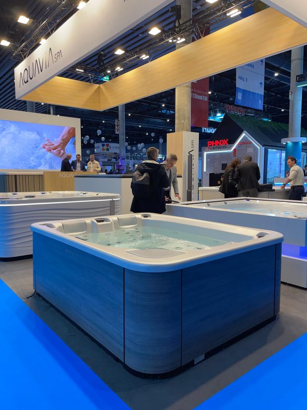 Stoisko targowe Aquavia Spa z prezentowanymi wannami hydromasażowymi i rozmawiającymi odwiedzającymi.