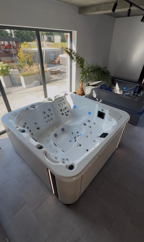 Biała wanna z hydromasażem z podświetleniem LED ustawiona w nowoczesnym salonie z dużym oknem.