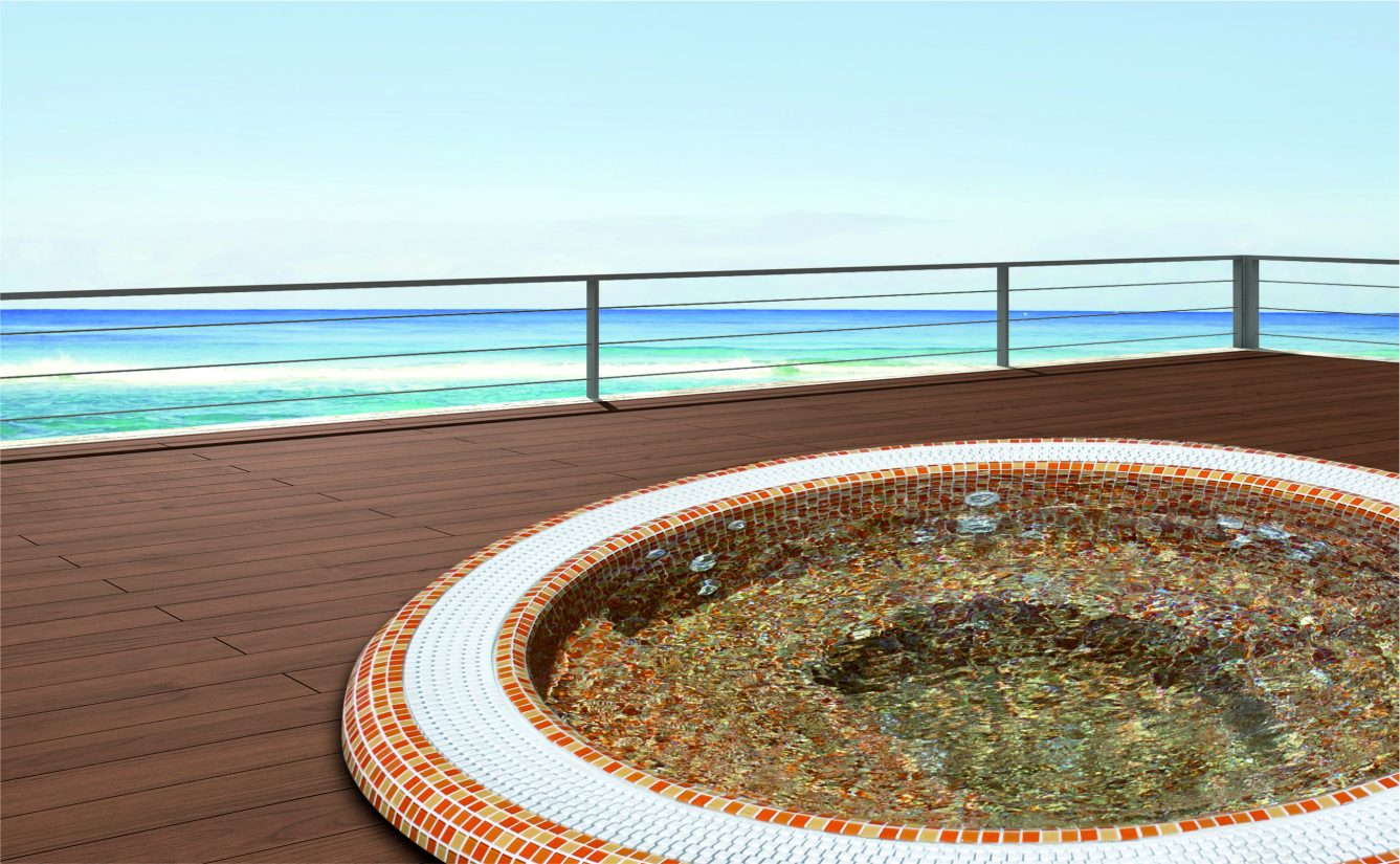 Okrągłe jacuzzi z mozaiką na drewnianym tarasie z widokiem na morze.