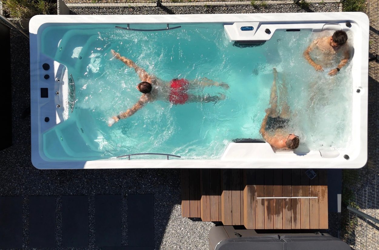 Trzech mężczyzn relaksujących się w zewnętrznym basenie z hydromasażem typu swim spa.